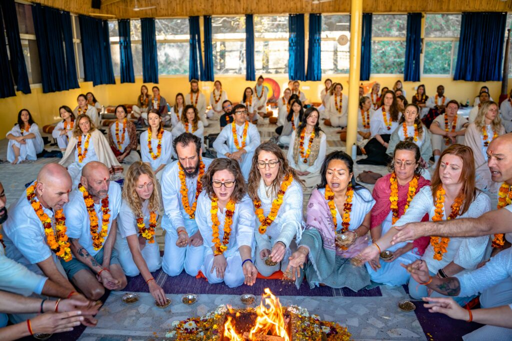 Group of people participating in a traditional fire ceremony in Rishikesh, India, wearing white clothes and garlands.