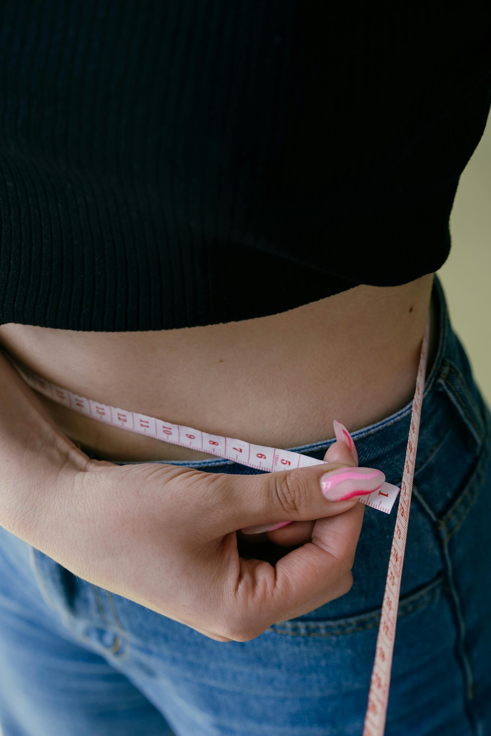 A woman measures her waist with a tape measure, focusing on fitness and weight management.